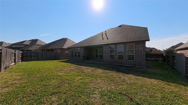 rear view of house featuring brick siding, a lawn, a fenced backyard, and roof with shingles