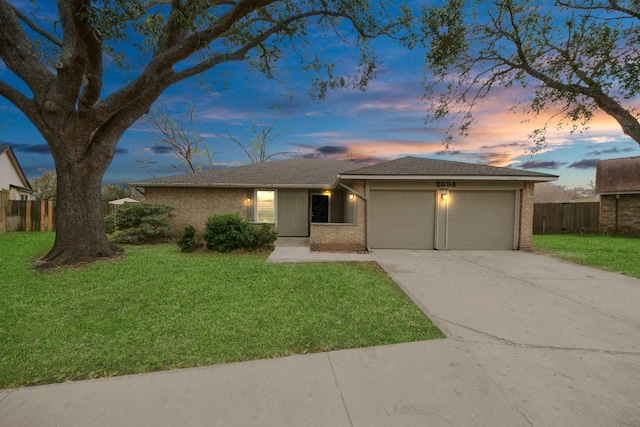 ranch-style house featuring fence, a yard, concrete driveway, an attached garage, and brick siding