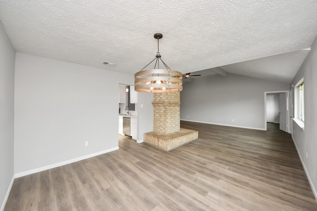 unfurnished living room with visible vents, a textured ceiling, wood finished floors, baseboards, and lofted ceiling