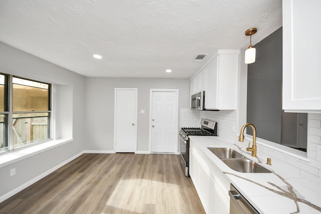 kitchen with visible vents, light wood-type flooring, stainless steel appliances, white cabinetry, and a sink