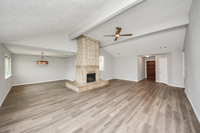 unfurnished living room featuring a brick fireplace, vaulted ceiling with beams, wood finished floors, and a textured ceiling