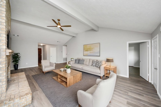 living area with visible vents, vaulted ceiling with beams, baseboards, a fireplace, and wood finished floors