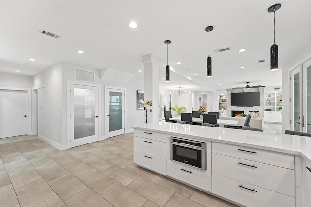 kitchen featuring a large fireplace, visible vents, open floor plan, and white cabinetry