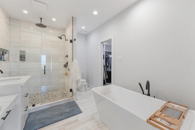 bathroom with a stall shower, a spacious closet, vanity, a freestanding tub, and recessed lighting