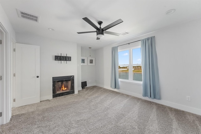 unfurnished living room with a lit fireplace, carpet, visible vents, and a ceiling fan