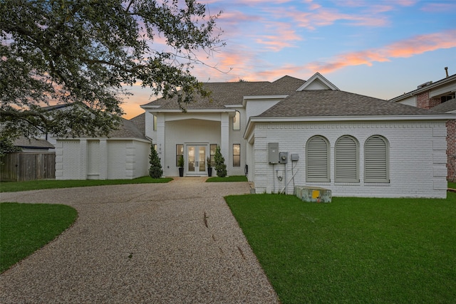 view of front of property with french doors, brick siding, a yard, roof with shingles, and driveway