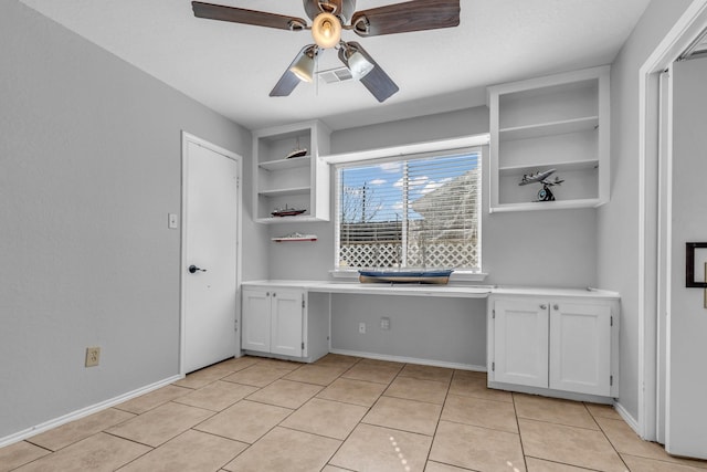 unfurnished office with light tile patterned floors, built in study area, a ceiling fan, and baseboards