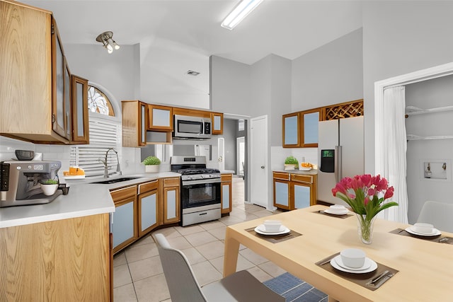 kitchen with light tile patterned floors, a towering ceiling, stainless steel appliances, light countertops, and a sink