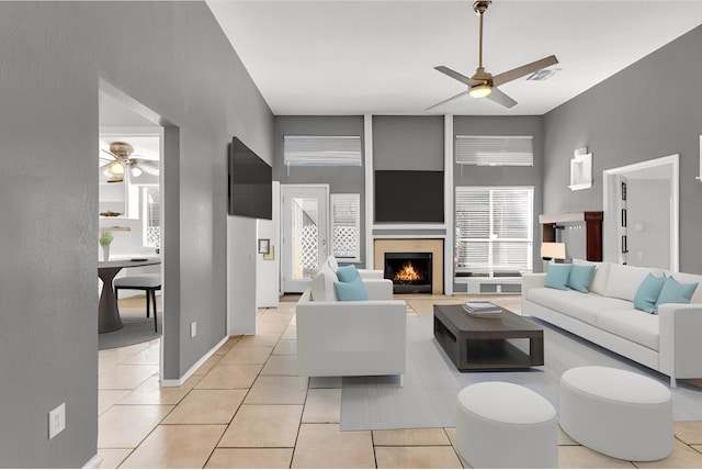 living area featuring visible vents, ceiling fan, a lit fireplace, and light tile patterned floors