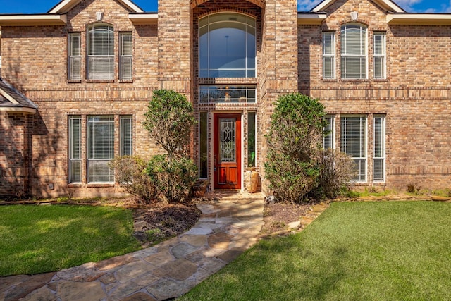 doorway to property with a lawn and brick siding