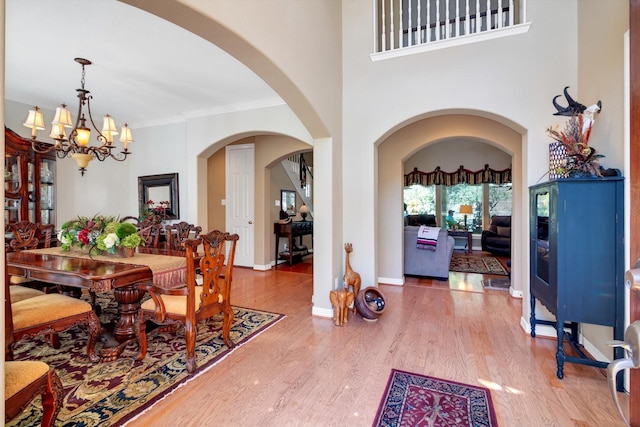 dining area with a chandelier, arched walkways, wood finished floors, baseboards, and crown molding