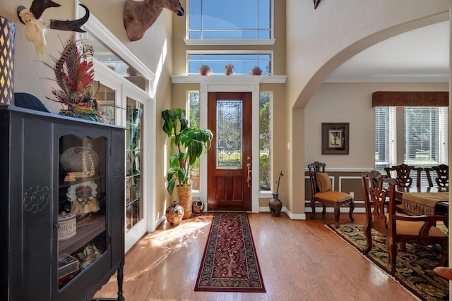 foyer entrance featuring arched walkways, a high ceiling, wood finished floors, baseboards, and crown molding