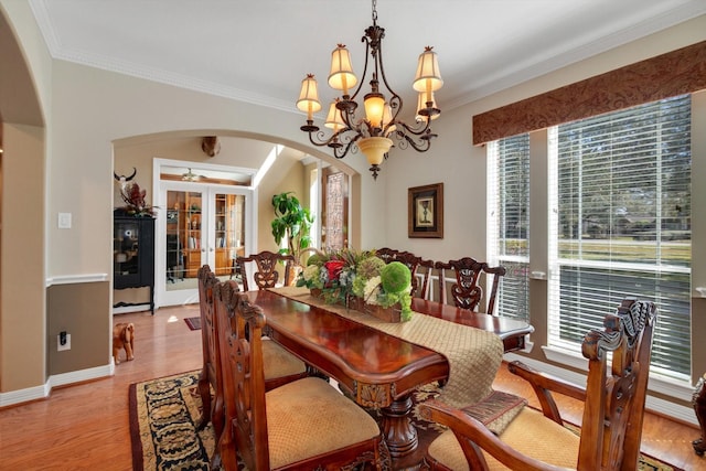 dining area featuring arched walkways, light wood-style flooring, ceiling fan with notable chandelier, baseboards, and ornamental molding