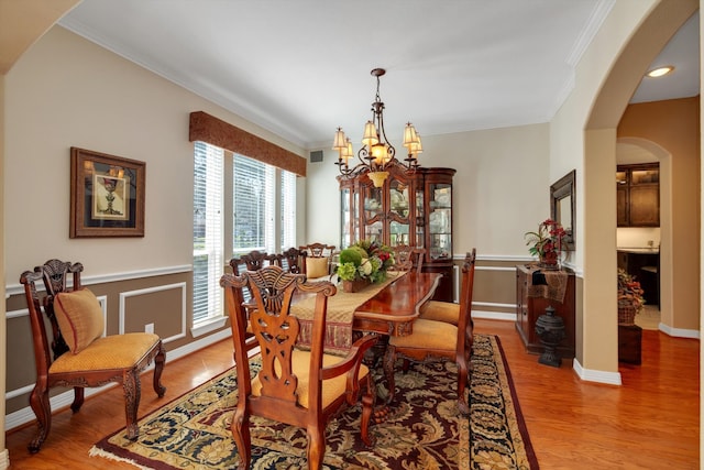 dining space with arched walkways, wood finished floors, baseboards, an inviting chandelier, and crown molding