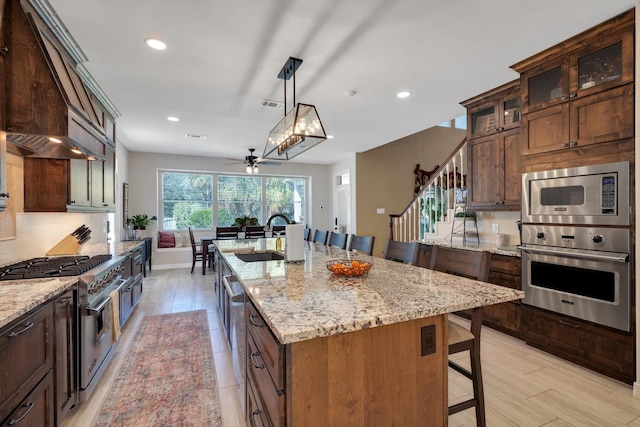 kitchen featuring a center island with sink, a breakfast bar area, appliances with stainless steel finishes, light stone counters, and a sink