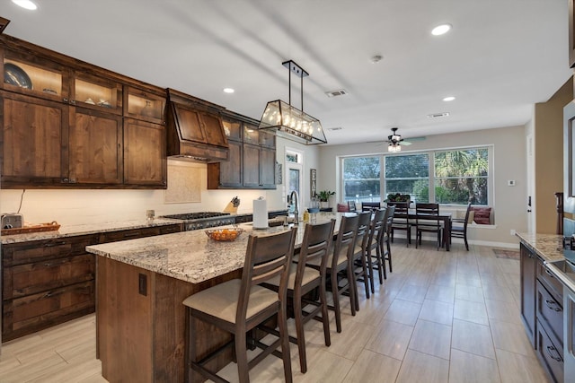 kitchen with stainless steel gas cooktop, visible vents, dark brown cabinets, light stone countertops, and premium range hood