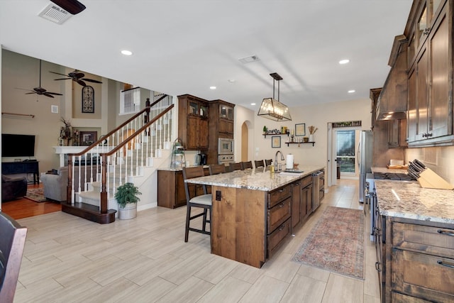 kitchen featuring arched walkways, visible vents, appliances with stainless steel finishes, a kitchen island with sink, and a sink