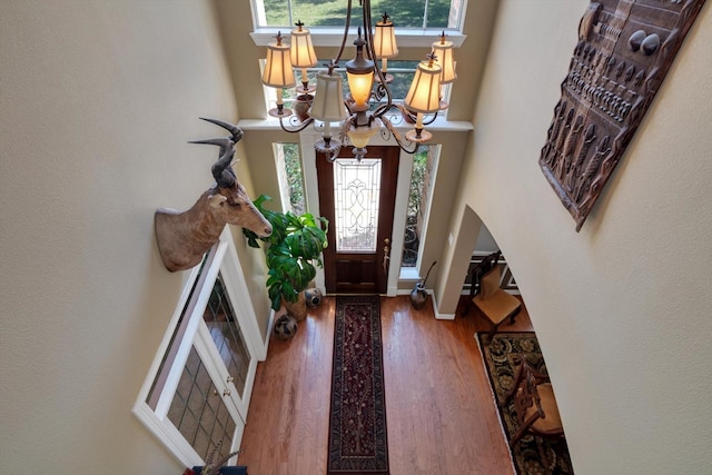 entryway featuring a chandelier, arched walkways, wood finished floors, and a towering ceiling