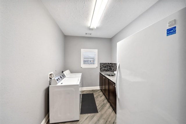 8133 N Fm 565th Rd, Baytown, TX 77523 - clothes washing area featuring a sink, washing machine and dryer, light wood-style floors, baseboards, and a textured ceiling