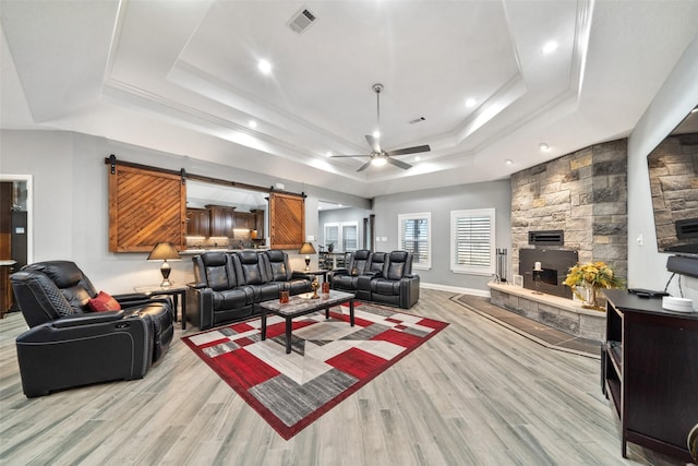 8133 N Fm 565th Rd, Baytown, TX 77523 - living area featuring a raised ceiling, a stone fireplace, visible vents, a ceiling fan, and light wood-style floors