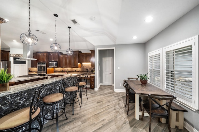 8133 N Fm 565th Rd, Baytown, TX 77523 - kitchen with dark brown cabinets, decorative backsplash, a breakfast bar, stainless steel appliances, and visible vents