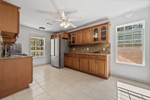 kitchen with brown cabinetry, freestanding refrigerator, dark stone counters, and a sink