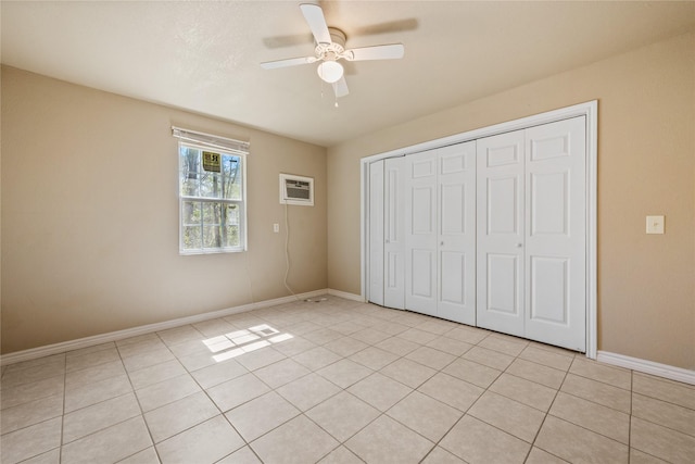 unfurnished bedroom with a closet, an AC wall unit, baseboards, and light tile patterned floors