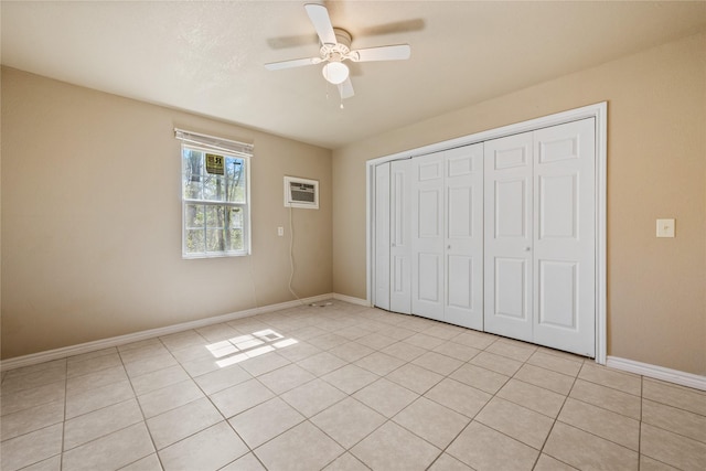 unfurnished bedroom with a ceiling fan, baseboards, a wall unit AC, light tile patterned floors, and a closet