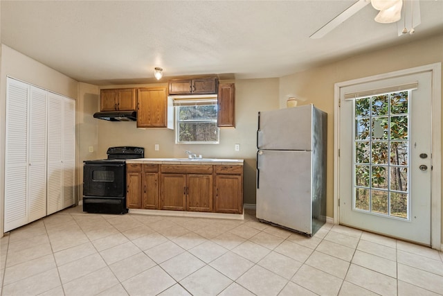 kitchen featuring brown cabinetry, black electric range, light countertops, freestanding refrigerator, and under cabinet range hood