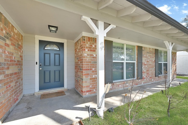 entrance to property featuring covered porch and brick siding