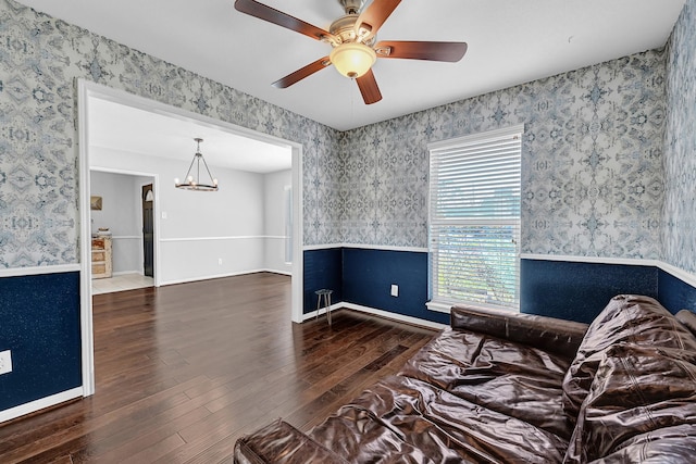 living area featuring ceiling fan with notable chandelier, wood finished floors, a wainscoted wall, and wallpapered walls