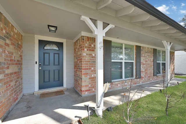 doorway to property with a porch and brick siding