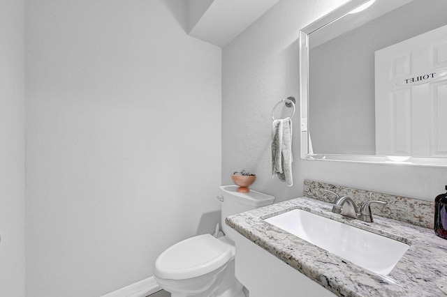 half bathroom featuring toilet, baseboards, and vanity