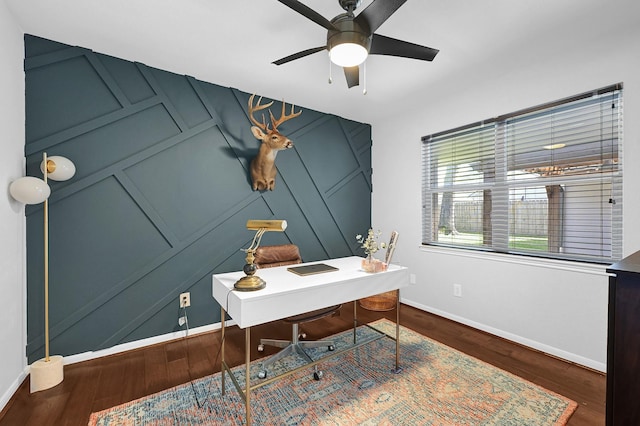 office area featuring baseboards, a ceiling fan, a decorative wall, and wood finished floors