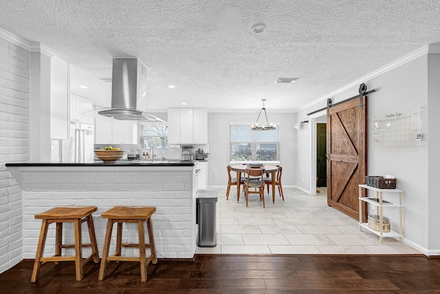 kitchen with a barn door, visible vents, white cabinets, island exhaust hood, and light wood-style floors