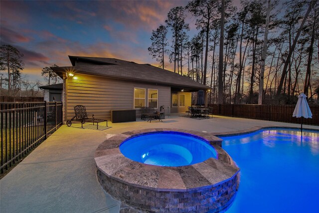 pool at dusk with a patio area, a fenced backyard, and a pool with connected hot tub