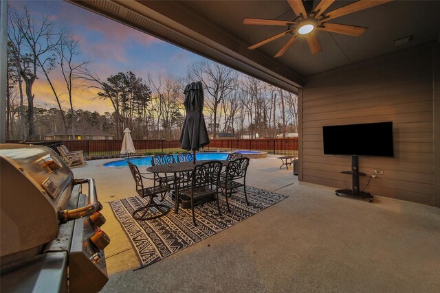 patio terrace at dusk with grilling area, a fenced backyard, a ceiling fan, and a fenced in pool