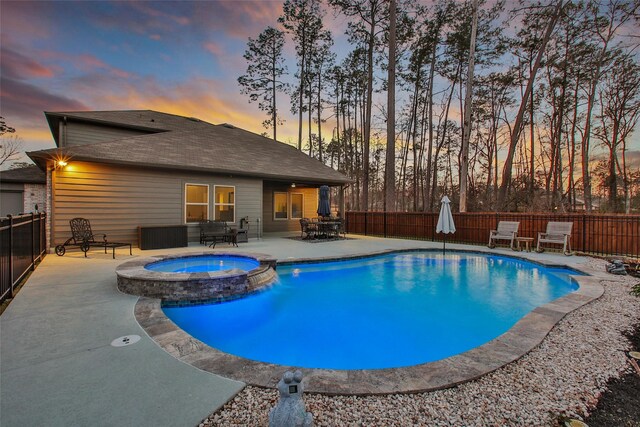 pool at dusk with a fenced backyard, a pool with connected hot tub, and a patio