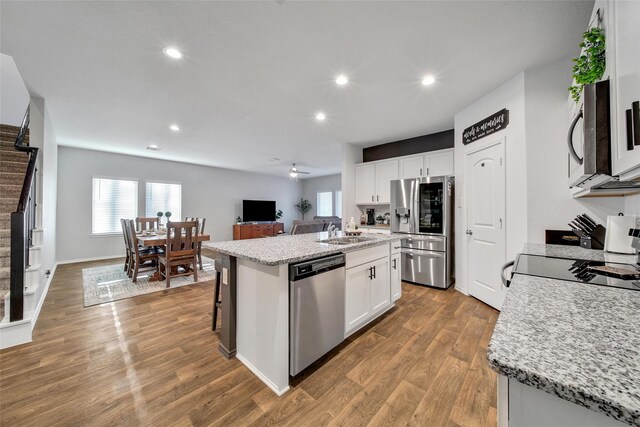 kitchen with appliances with stainless steel finishes, a kitchen island with sink, a sink, white cabinetry, and wood finished floors