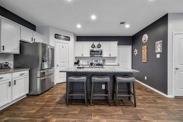 kitchen featuring a breakfast bar area, stainless steel appliances, visible vents, dark wood-type flooring, and light stone countertops