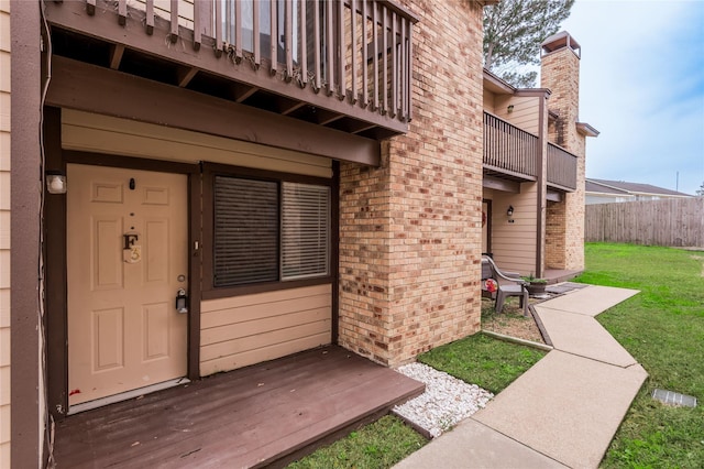 property entrance with a balcony, a yard, fence, and brick siding