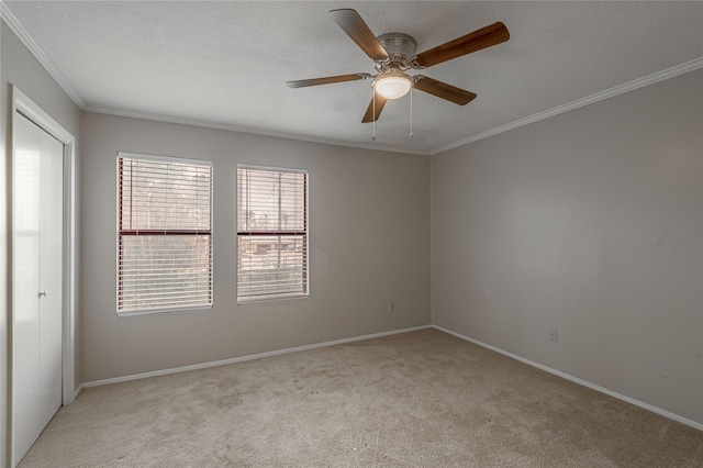 spare room featuring a textured ceiling, ceiling fan, light colored carpet, baseboards, and ornamental molding