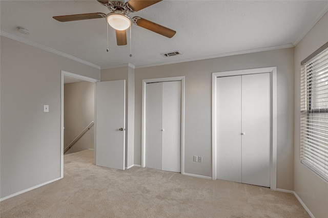 unfurnished bedroom with ornamental molding, two closets, visible vents, and light colored carpet