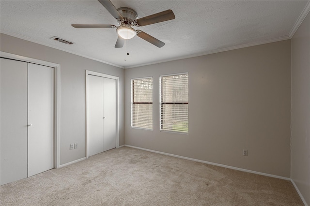 unfurnished bedroom with visible vents, ornamental molding, carpet, a textured ceiling, and multiple closets