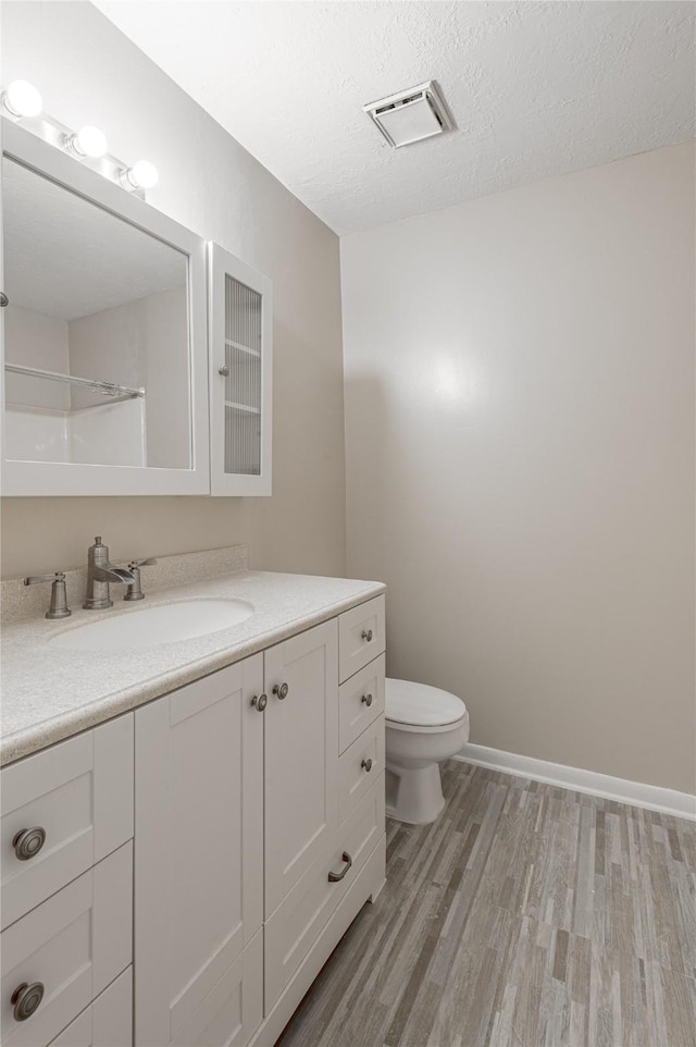 bathroom featuring visible vents, toilet, a textured ceiling, vanity, and wood finished floors