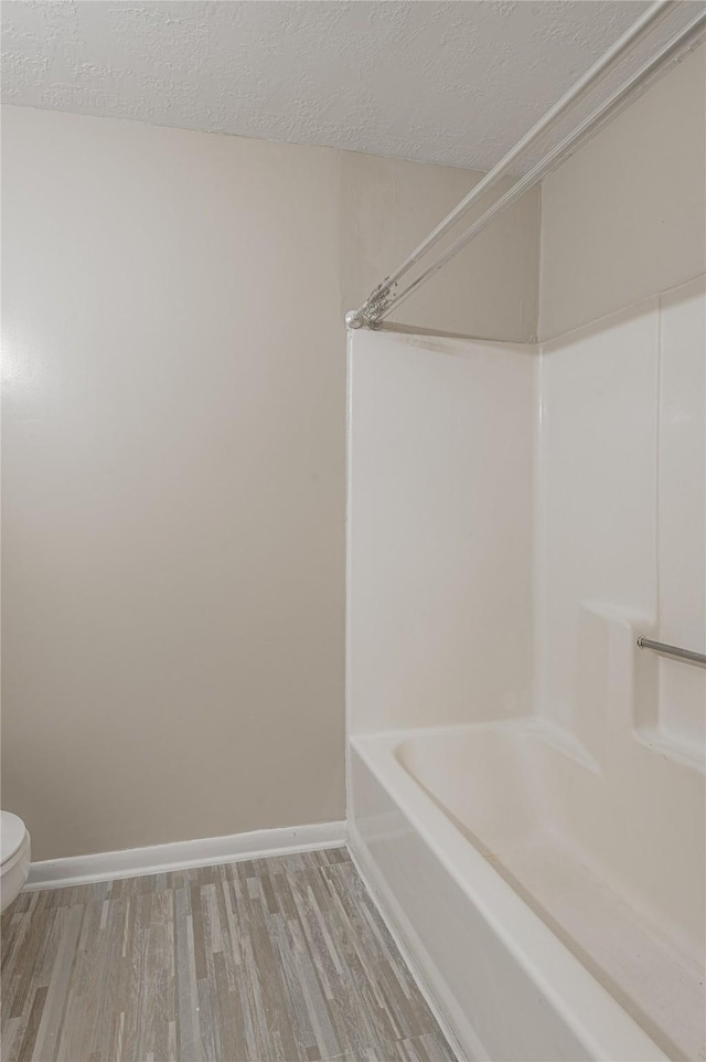 full bath with shower / washtub combination, toilet, a textured ceiling, wood finished floors, and baseboards