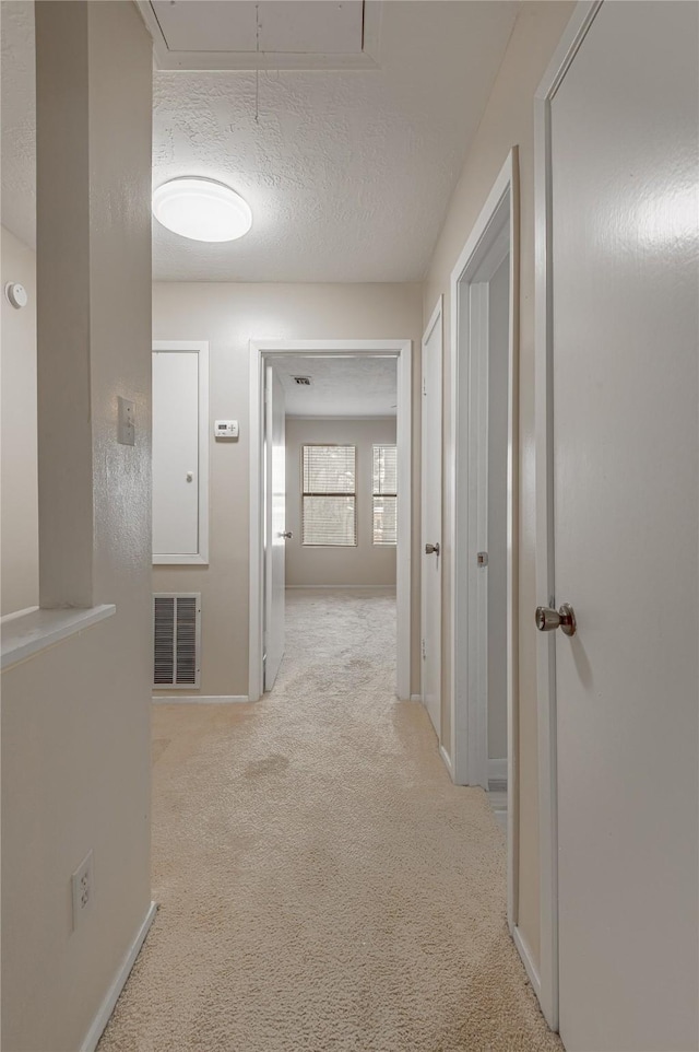 hallway with visible vents, attic access, light carpet, a textured ceiling, and baseboards