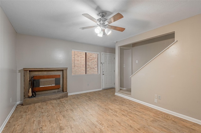 unfurnished living room with a ceiling fan, a fireplace with raised hearth, baseboards, and wood finished floors