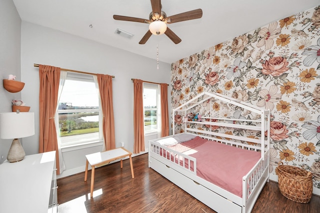 bedroom with visible vents, an accent wall, a ceiling fan, wood finished floors, and wallpapered walls