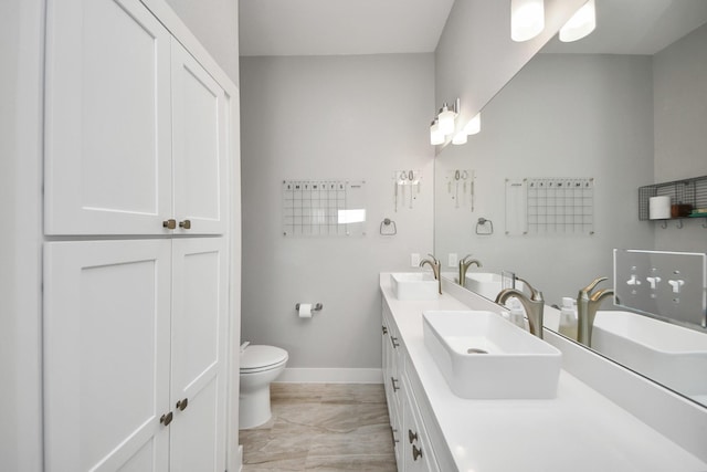 bathroom featuring baseboards, a sink, toilet, and double vanity